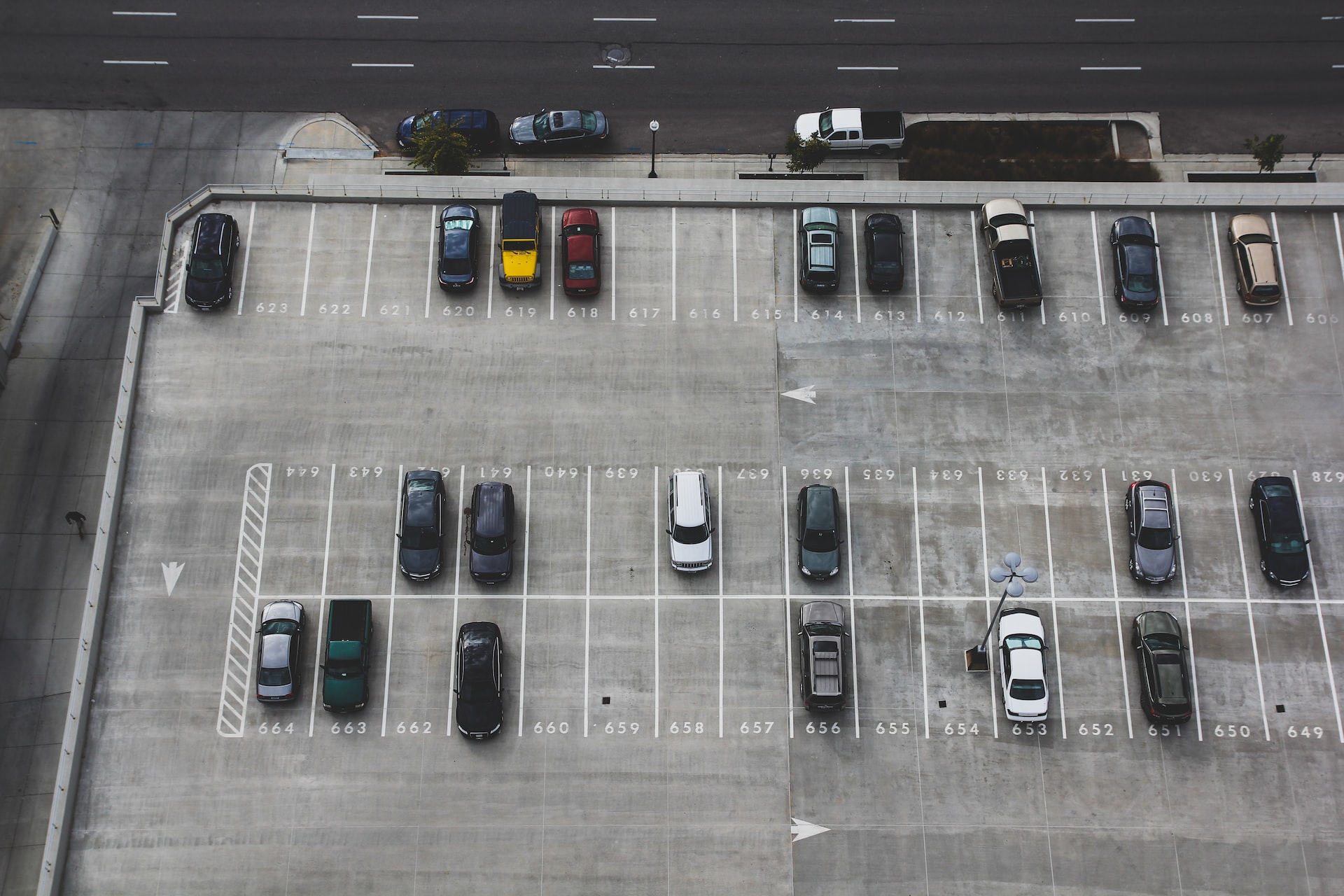 Aerial view of a spacious open parking lot, with 21 vehicles parked on white-painted numbered parking slots