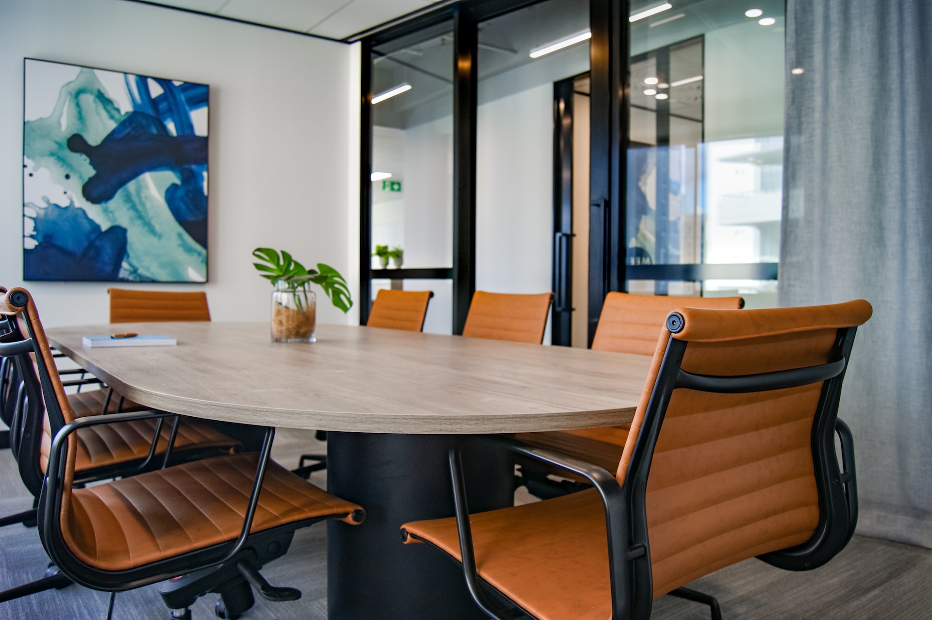 A PR firm meeting room with glass doors, eight-seater oblong-shaped table and abstract painting on the wall
