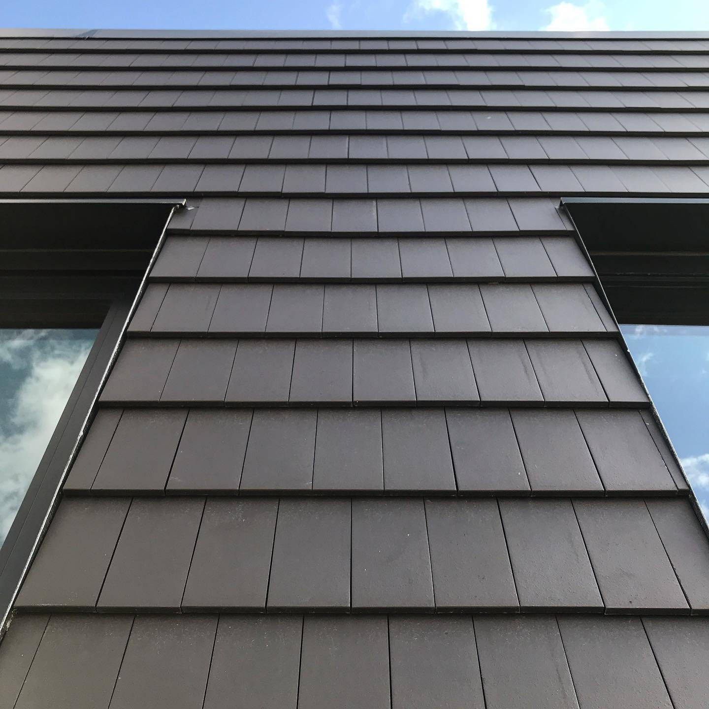View from a lower level of a part of a house with rectangular black rainscreens installed vertically