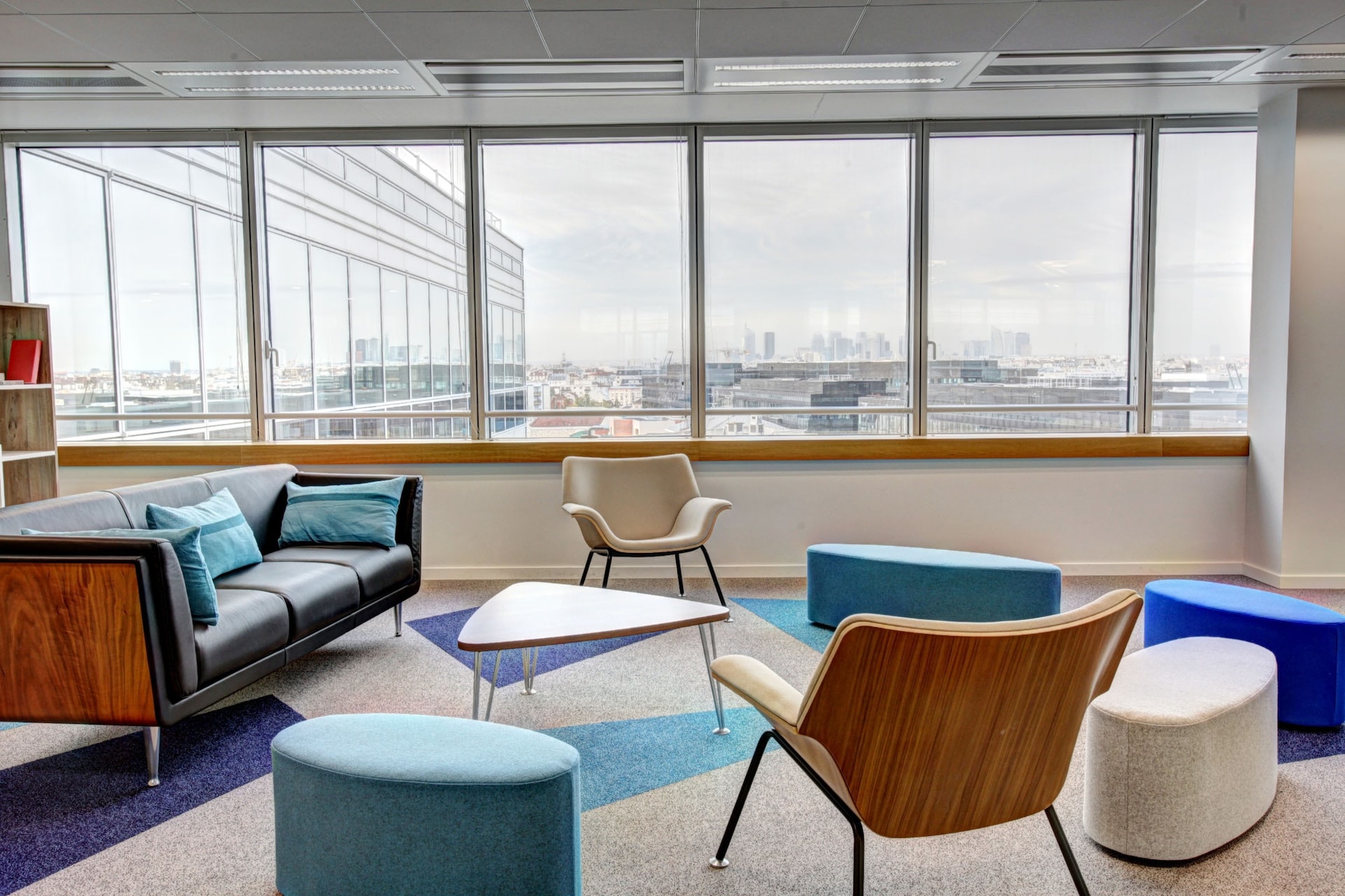 A PR firm’s office lounge with couch, chairs, and a small table on a carpet and a row of glass windows