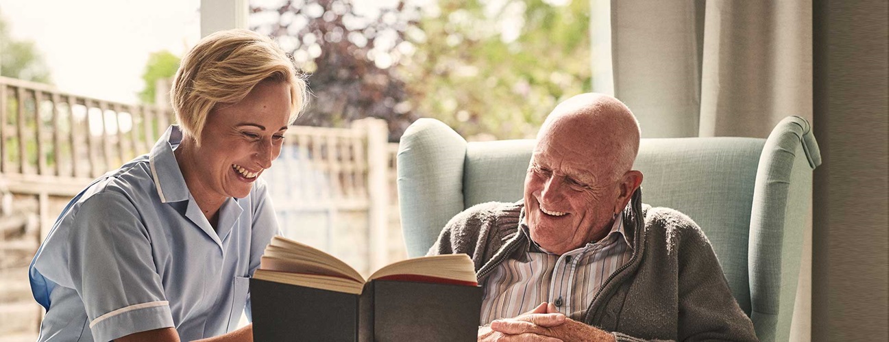 A caregiver and a patient reading a book and laughing