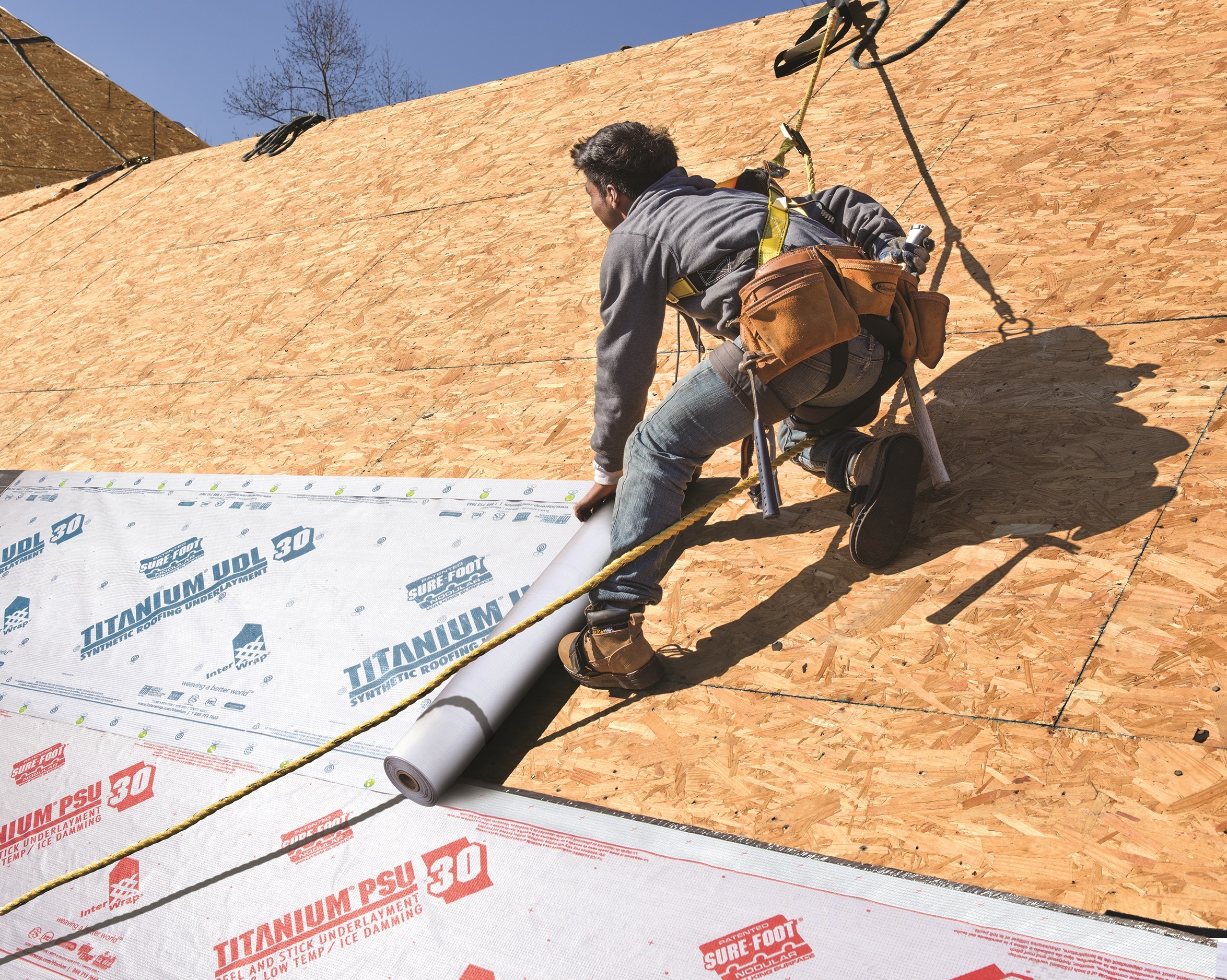 A worker installing synthetic underlayment on roof