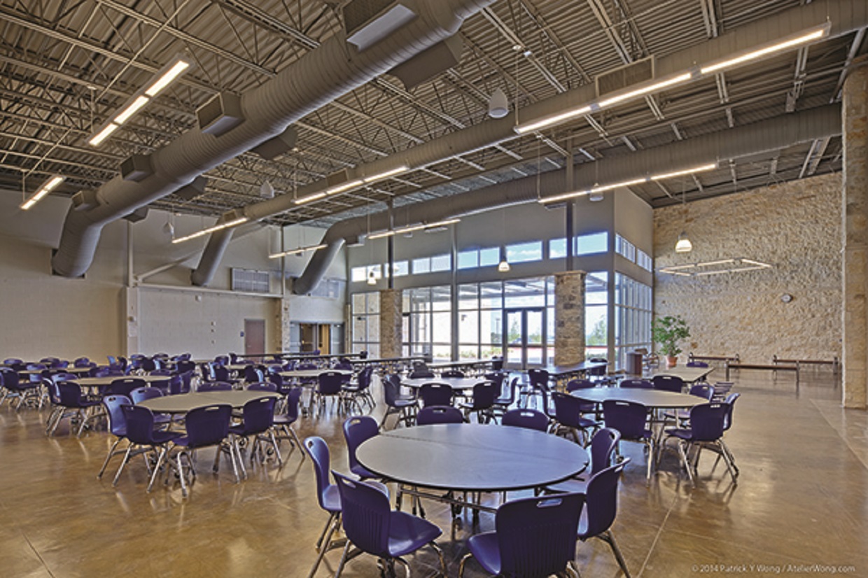 An empty Lago Vista High School lounging area, with huge exposed pipelines, white round tables and blue chairs