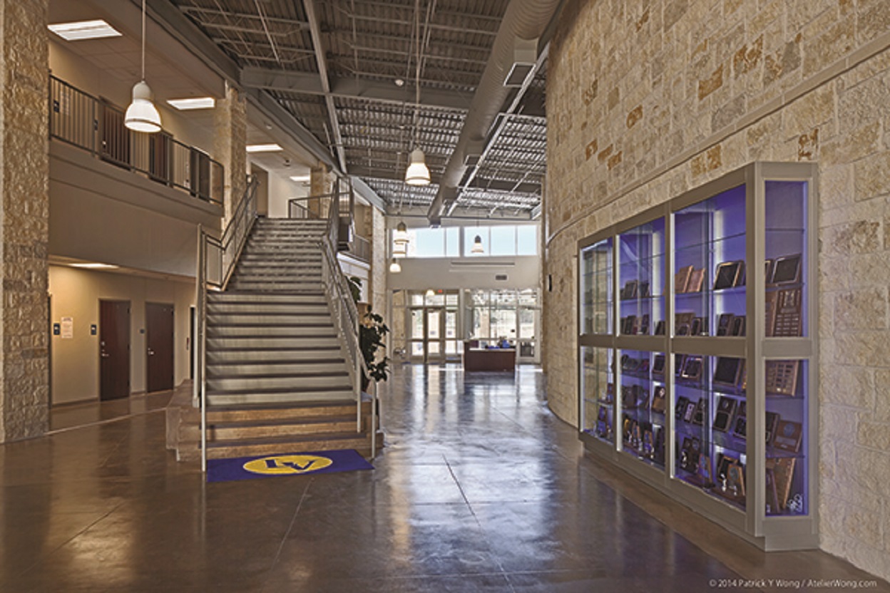 Inside Lago Vista High School, with exposed roof, huge tiled floor, brick walls, and stairs with metal handrails