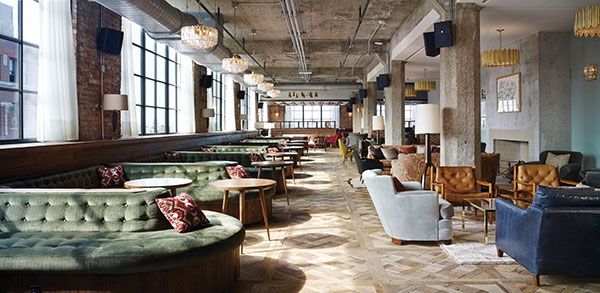 Sunlight streams inside Soho House Chicago through its large windows, with rows of long couches and hanging lights